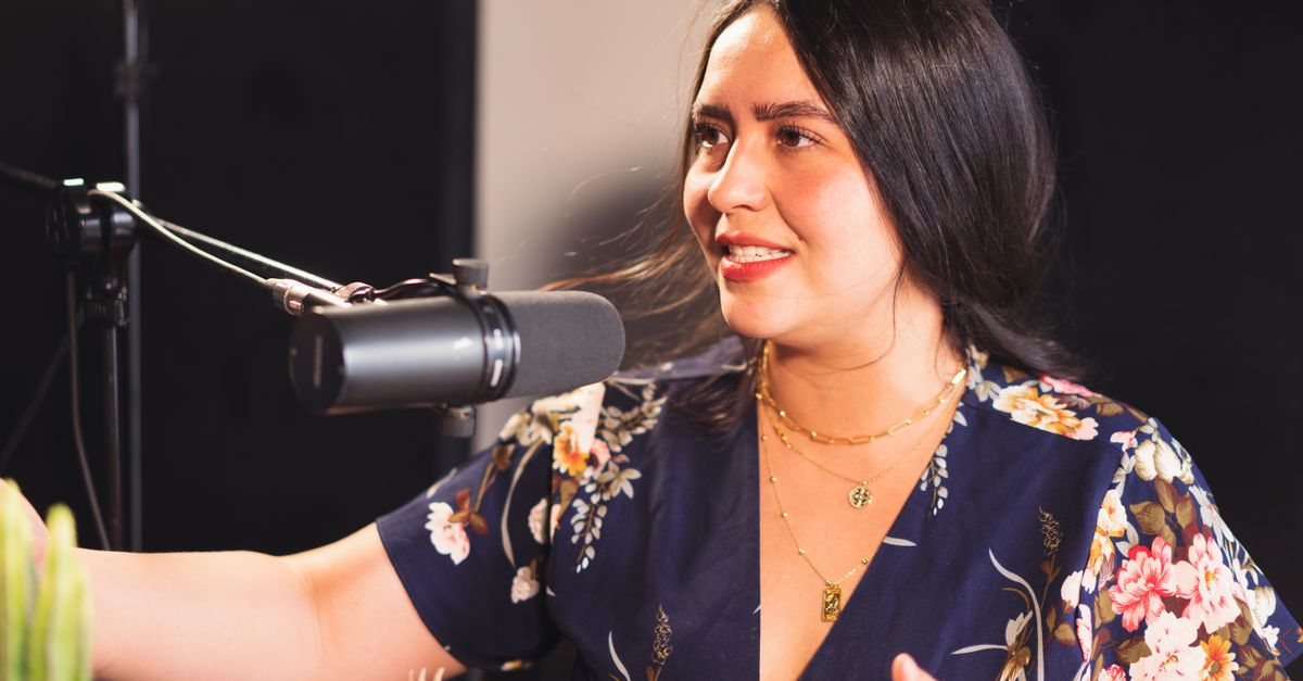 Portrait of a woman hosting a podcast, speaking into a microphone indoors.